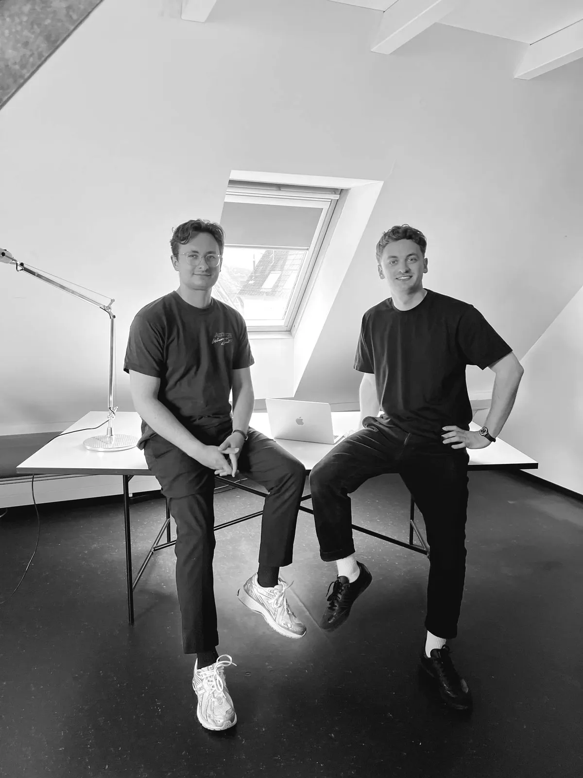 Moritz and Felix Strobel sitting on a desk in their studio (black and white photo)