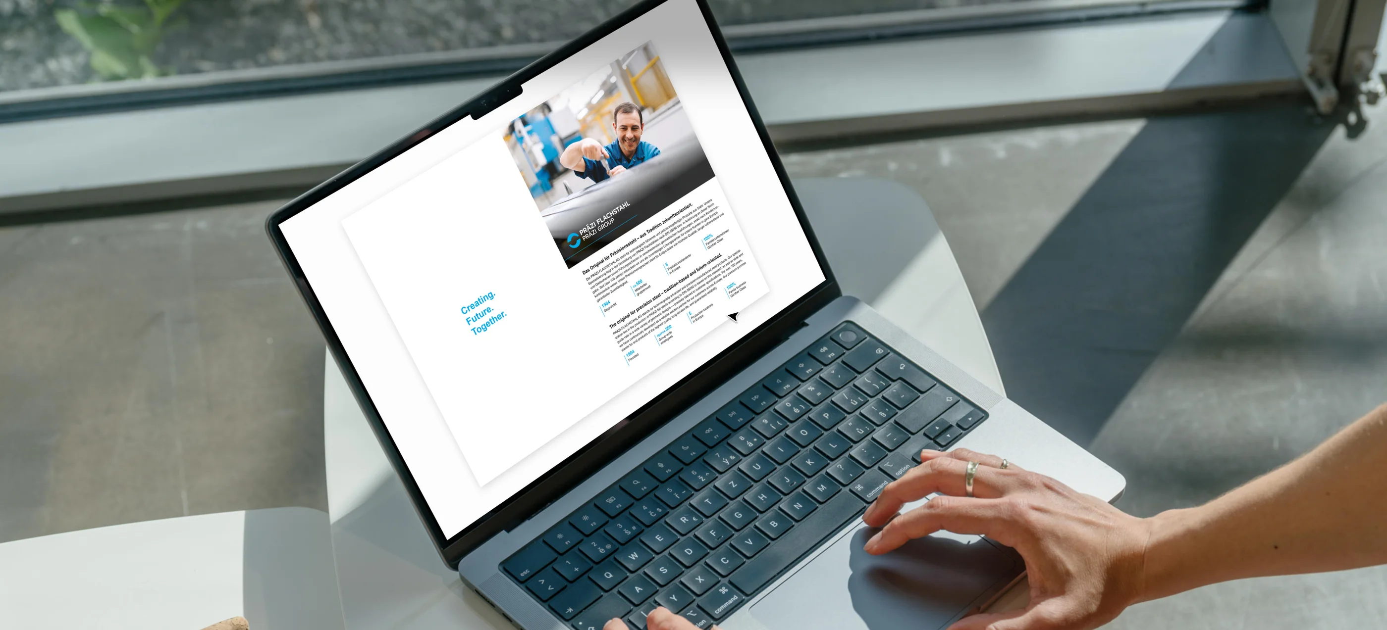 Hands on a laptop showing a digital PRÄZI Flachstahl brochure with the line “Creating. Future. Together.”